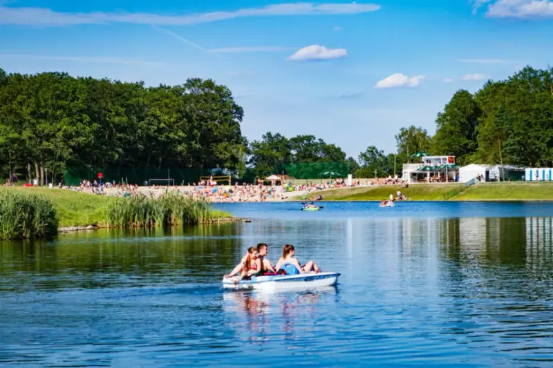 Rodzina na rowerku wodnym na jeziorze, plaża pełna ludzi, las i budynki w tle. Idealne miejsce gdzie nad wodę Dolny Śląsk.