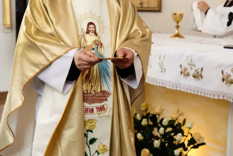 Kapłan w złotej szacie z wizerunkiem Jezusa trzyma hostię. Czy dzisiaj trzeba iść do kościoła?