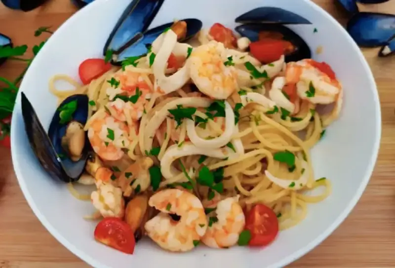 Pyszne linguini z krewetkami, kalmarami i małżami, ozdobione pomidorkami i natką pietruszki.