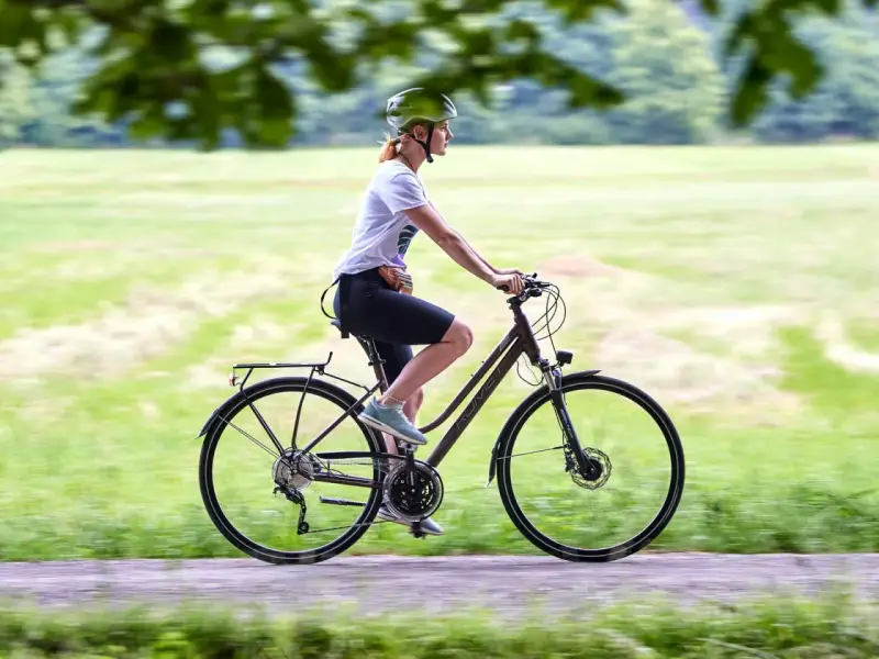 Kobieta w kasku jedzie na rowerze trekkingowym po ścieżce w parku.
