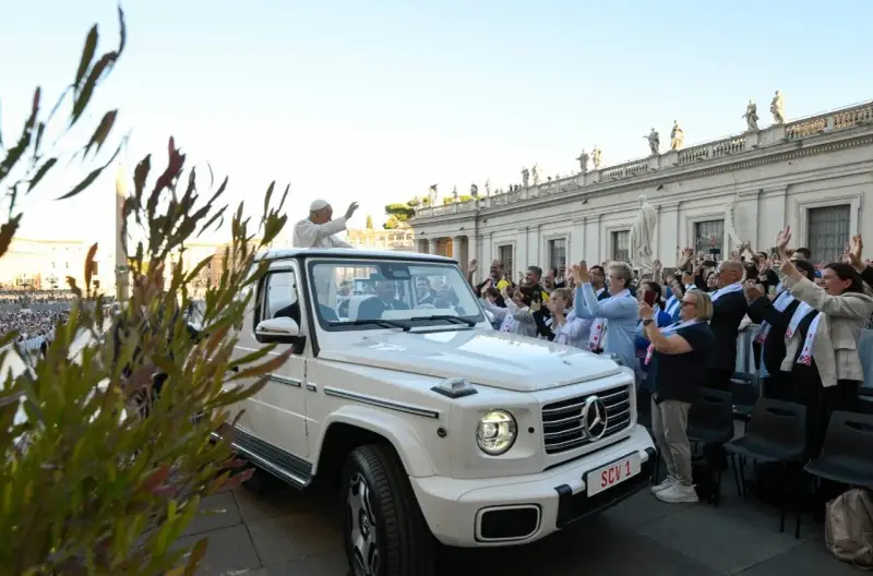 Papież Franciszek, mimo swojego vatican wiek, pozdrawia wiernych z białego mercedesa. Tłum wiwatuje, a niektórzy robią zdjęcia.