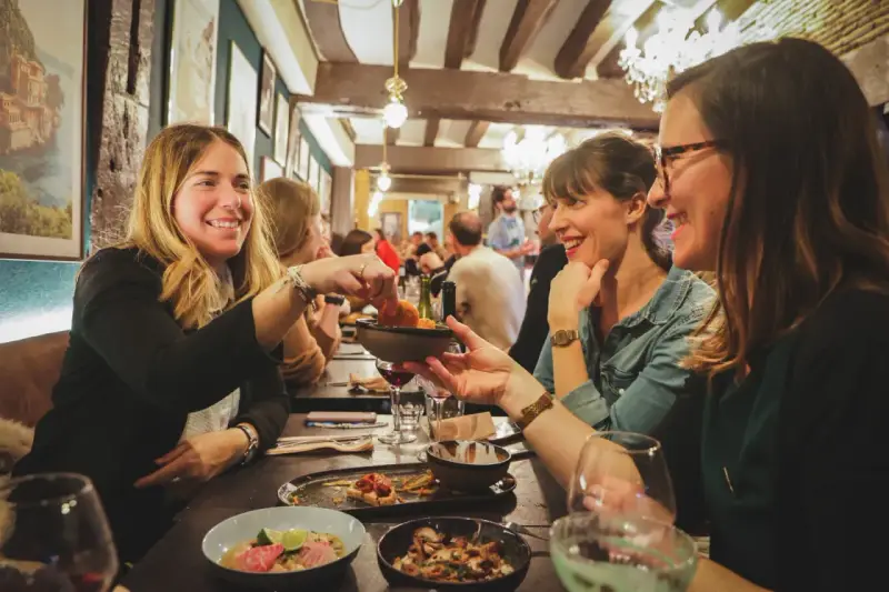 Amies joyeuses partageant des tapas dans un resto ouvert le dimanche à Rennes. Ambiance chaleureuse et conviviale.