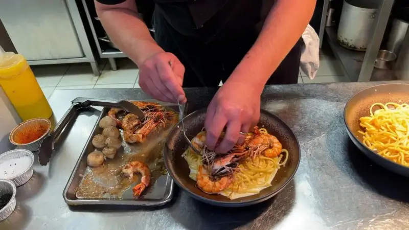 Un chef prépare des pâtes aux crevettes et pétoncles, un plat savoureux de cuisine de terroir.