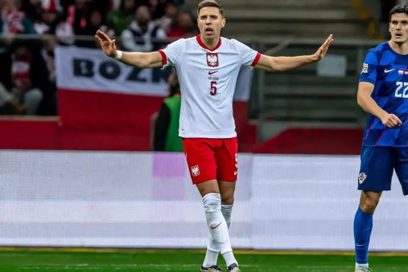 Piłkarz w białej koszulce z orłem, numer 5. Jan Bednarek po kontuzji wraca do gry, gestem prosi o spokój.