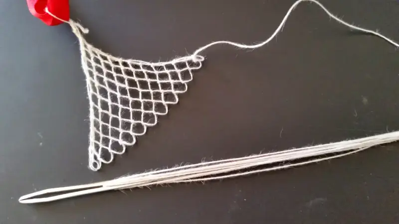 Un ago con filo bianco e un pezzo di rete a maglie, un tipo di ricamo eseguito su una rete a maglie, con un nastro rosso in alto.