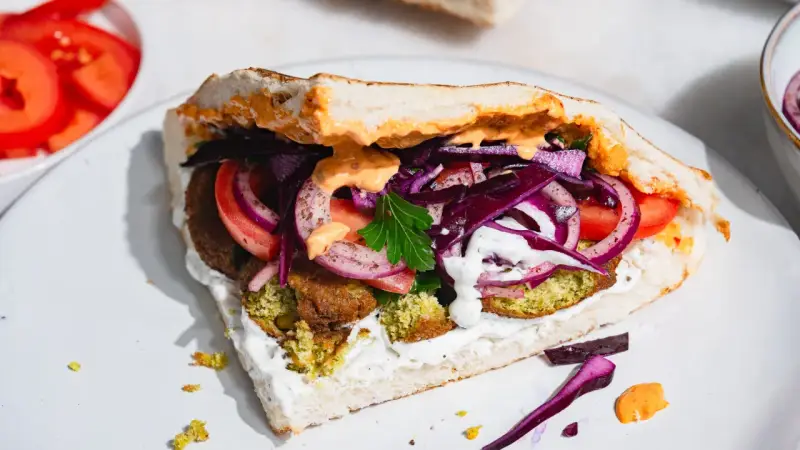 Pyszny falafel kebab w bułce z pomidorami, czerwoną cebulą, kapustą i sosami.