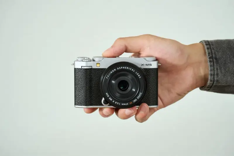 Mano sujetando una cámara Fujifilm X-M5 plateada y negra, lista para capturar momentos.