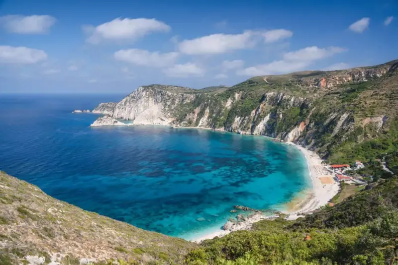Malownicza zatoka z turkusową wodą i piaszczystą plażą, otoczona stromymi, zielonymi klifami. To idealne miejsce na wypoczynek na wyspie na Morzu Jońskim.