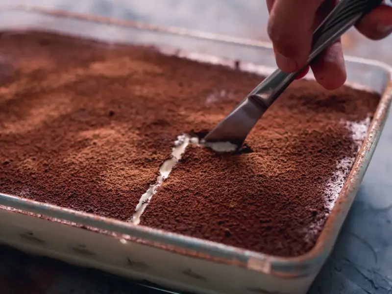 Kto pyta, czy mascarpone jest fit, gdy widzi tak kuszące tiramisu? Nóż kroi deser, odsłaniając kremową warstwę.