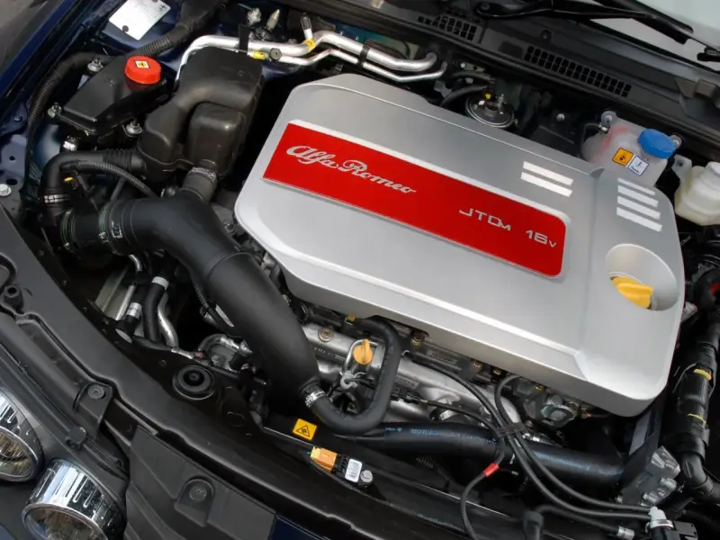 Silnik Alfa Romeo 1.9 JTD 16V z widocznym srebrnym deklom z czerwonym pasem i napisem.