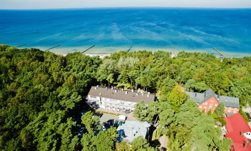 Widok z lotu ptaka na hotel otoczony lasem, z widokiem na morze. Idealne miejsce na wakacje, sprawdź nasz tui kod rabatowy!