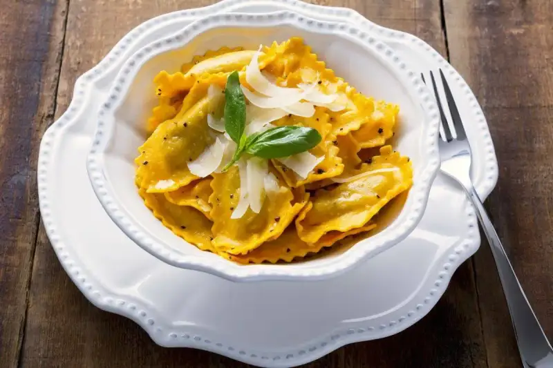 Un piatto invitante di tortelli di zucca, guarniti con scaglie di parmigiano e una fogliolina di basilico, pronti per essere gustati.