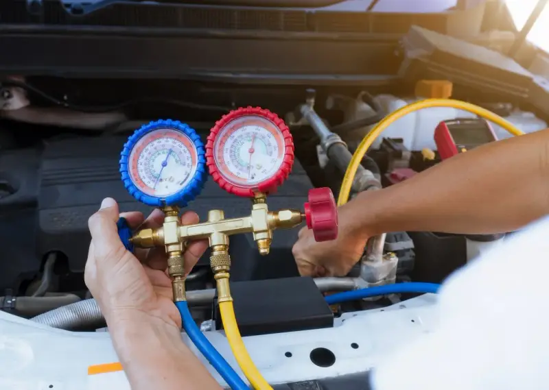 A mechanic uses a manifold gauge set to check for a freon leak in a car's AC system.