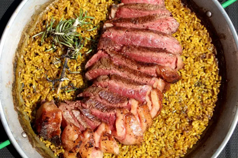 Arroz amarillo con chuletón a la parrilla y romero en paellera.