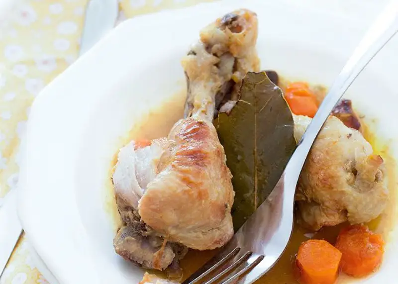 Delicioso pollo guisado con zanahorias y hoja de laurel en un plato blanco, listo para ser disfrutado.