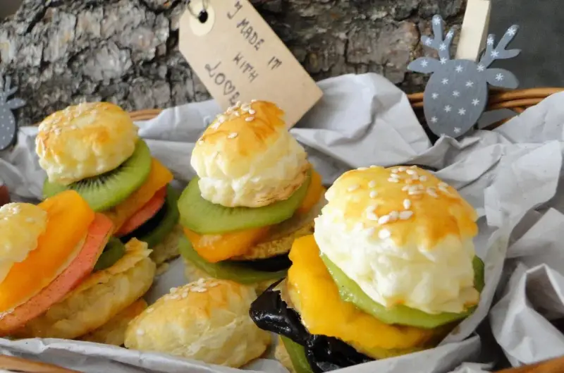Mini burgery z ciasta francuskiego z owocami: kiwi, mango, brzoskwinia i różowa wędlina. Wyglądają jak małe dzieła sztuki.