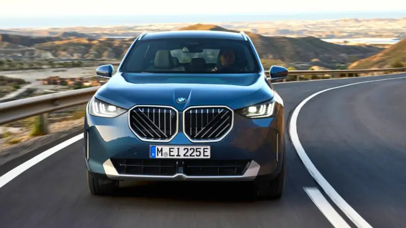 Nowy **BMW X3 2025** w kolorze granatowym jedzie krętą drogą pośród pustynnych krajobrazów.