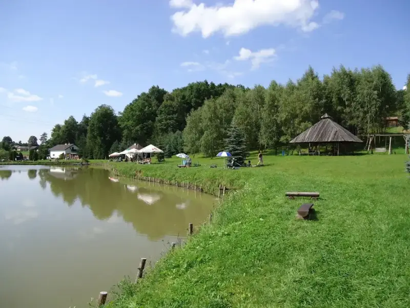 Malownicze dzikie łowiska Małopolska: spokojna woda, zielone wzgórza, drewniana altana i miejsca do wypoczynku.