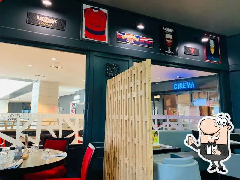 Ambiance chaleureuse à la trattoria Ibos, avec des décorations de rugby et de bière. Une enseigne "CINEMA" brille au loin.