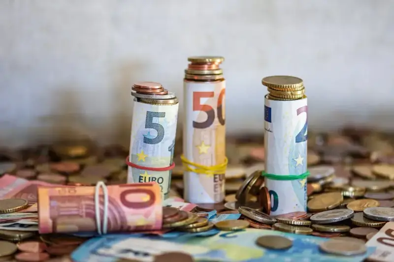 Zwijane banknoty euro i monety, symbolizujące kwotę darowizny wolną od podatku, tworzą stosy na tle innych monet.