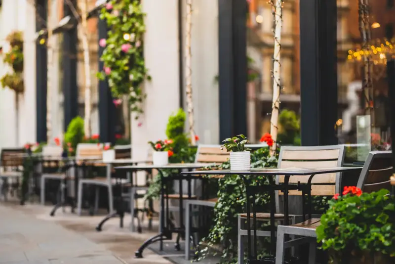 Mesas y sillas vacías en la terraza de un restaurante, adornadas con plantas y flores. Un lugar acogedor, listo para recibir clientes tras obtener las licencias de restaurantes.