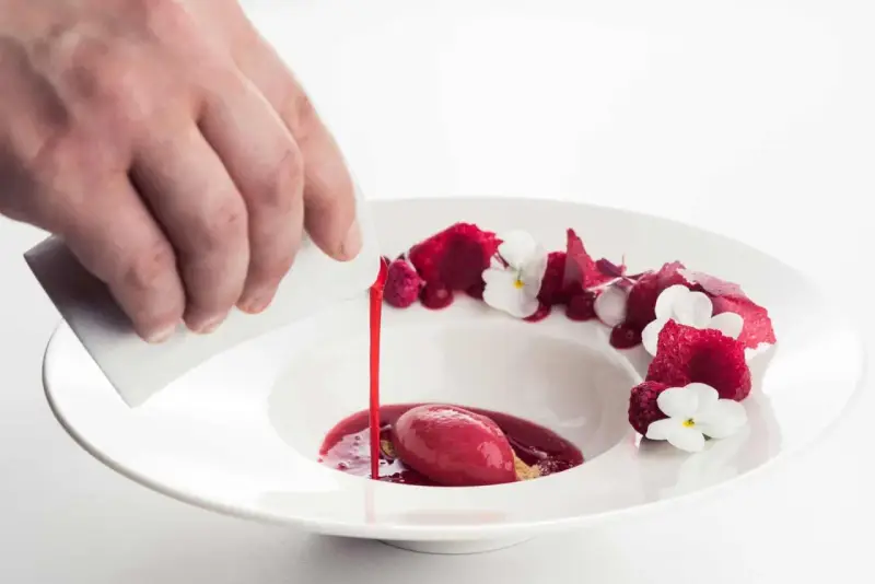 Wykwintny deser w restauracji z gwiazdką Michelin: malinowy sorbet z sosem i jadalnymi kwiatami, polany przez kucharza.