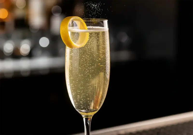 Ett glas French 75 med bubblor och citronskal. En klassisk drink med en intressant french 75 historia.