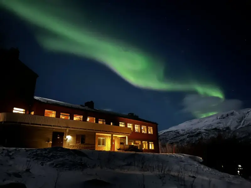 Norrsken över ett snötäckt landskap med ett hus. Perfekt för kiruna sightseeing turer.