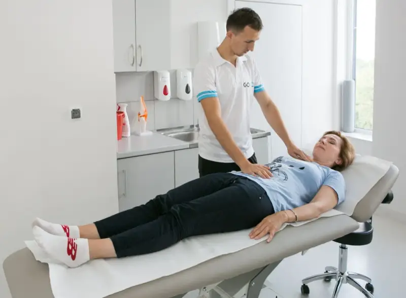 Fizjoterapeuta pomaga pacjentce w ćwiczeniach oddechowych, kładąc dłonie na jej klatce piersiowej i brzuchu.