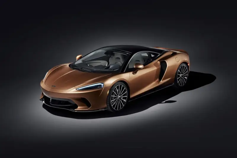 Elegancki, miedziany McLaren GT z czarnym dachem i felgami, prezentujący swoje sportowe linie na ciemnym tle.