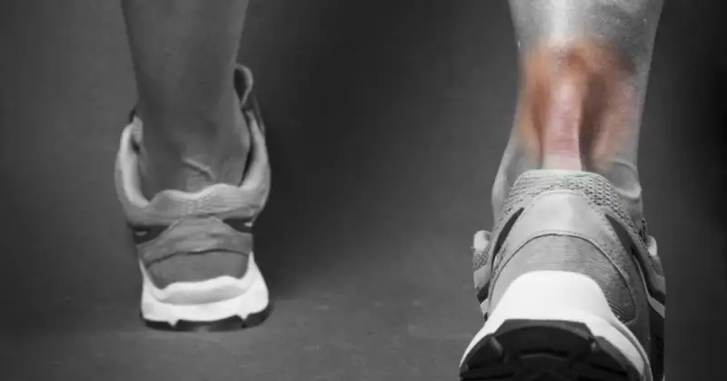 Ból w pięcie i łydce sugeruje zapalenie ścięgna Achillesa. Widok z tyłu na nogę w bucie sportowym, z zaczerwienionym obszarem.
