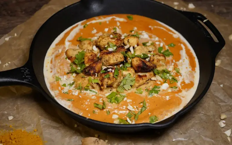 Ein authentisches Butter Chicken Rezept original in einer Gusseisenpfanne, garniert mit Koriander und gehackten Mandeln.