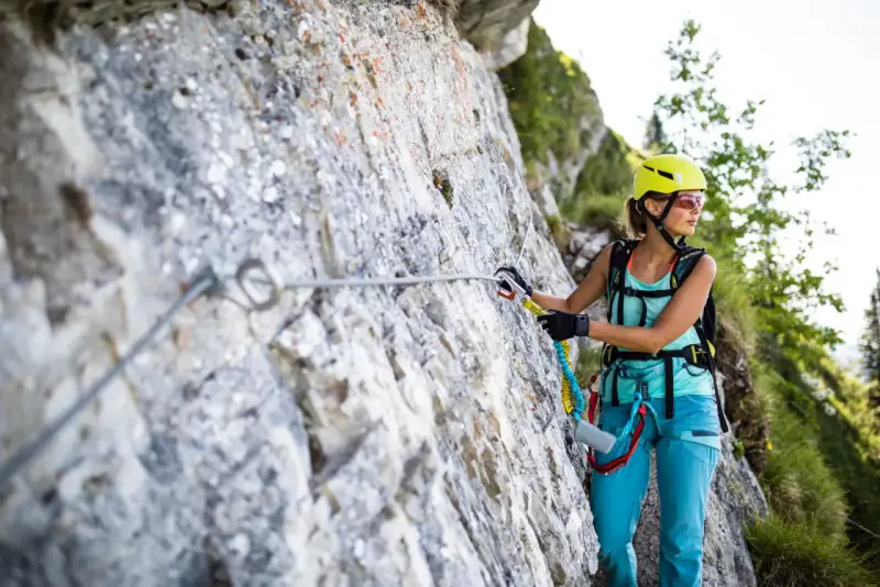 Kobieta w kasku i sprzęcie wspinaczkowym pokonuje via ferrata polska. Wspinaczka po skalnej ścianie z liną asekuracyjną.