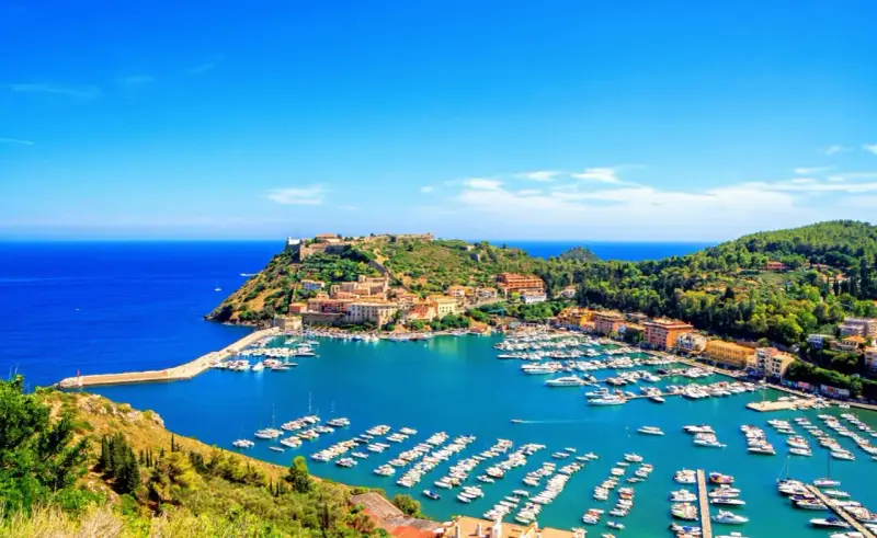 Porto Ercole, con le sue splendide spiagge e il porto pieno di barche, incanta sotto un cielo azzurro.