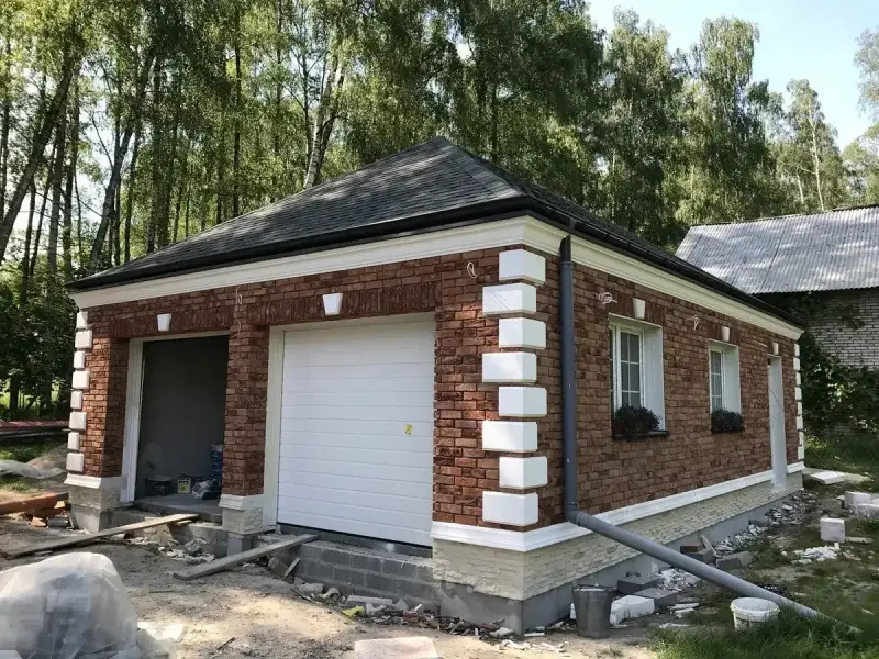 Nowy garaż z cegły z białym gzymsem i ozdobnymi elementami.