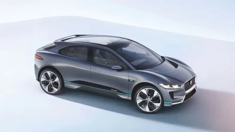 Elegancki, szary Jaguar I-PACE, niczym czarny jaguar gotowy do skoku, prezentuje swoją aerodynamiczną sylwetkę na jasnym tle.