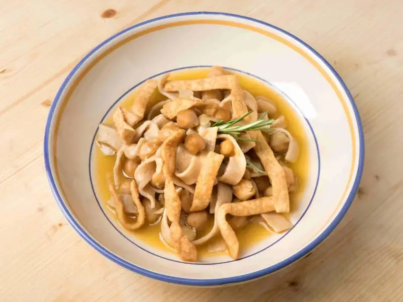 Un piatto di ciceri e tria, pasta fresca con ceci e sfoglie fritte, guarnito con rosmarino.