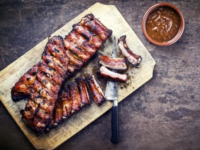 Soczyste żeberka w miodzie, grillowane do perfekcji, podane na desce z sosem.