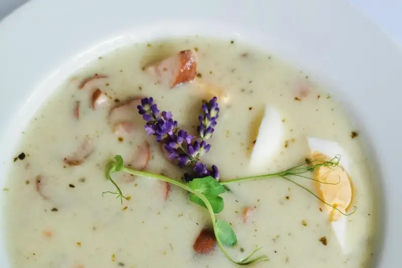 Aromaticzny żurek z kiełbasą i jajkiem, ozdobiony gałązką lawendy i kiełkami.
