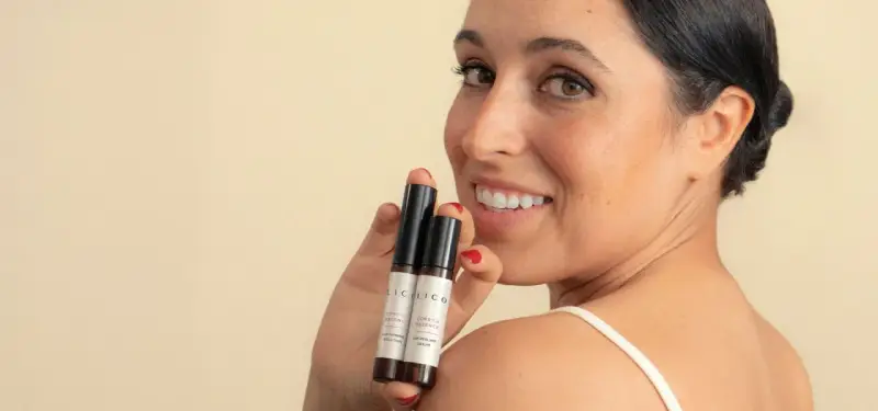 Mujer sonríe mostrando dos pequeños frascos, uno dice "Lip Peeling Serum", ideal para saber como exfoliar los labios.