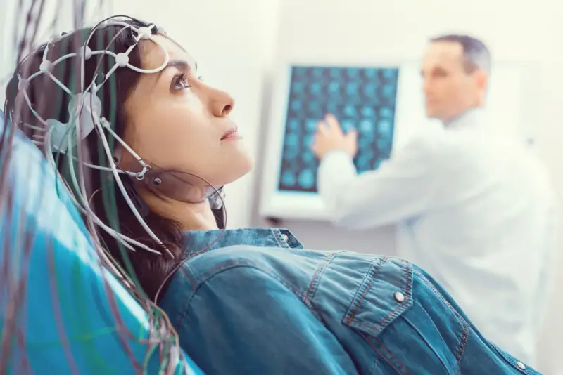 Kobieta z elektrodami na głowie podczas badania VEP. Lekarz analizuje wyniki na ekranie.
