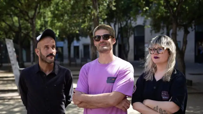 Miembros de Els Catarres posan al aire libre. El hombre de la izquierda lleva gorra y camisa negra. El del centro, gafas de sol y camiseta lila. La mujer de la derecha, gafas y camiseta negra.