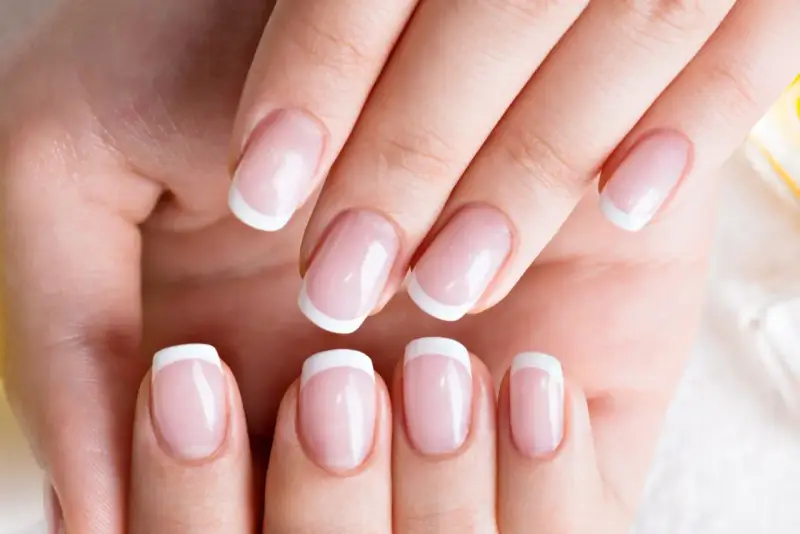 Dłonie z idealnym french manicure, gdzie białe końcówki paznokci lśnią jak tytanowe paznokcie.