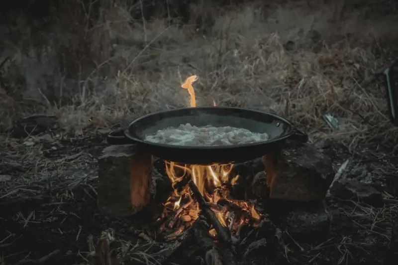 Cuisine en plein air sur un réchaud rocket stove improvisé. Une poêle cuit des aliments sur un feu vif.
