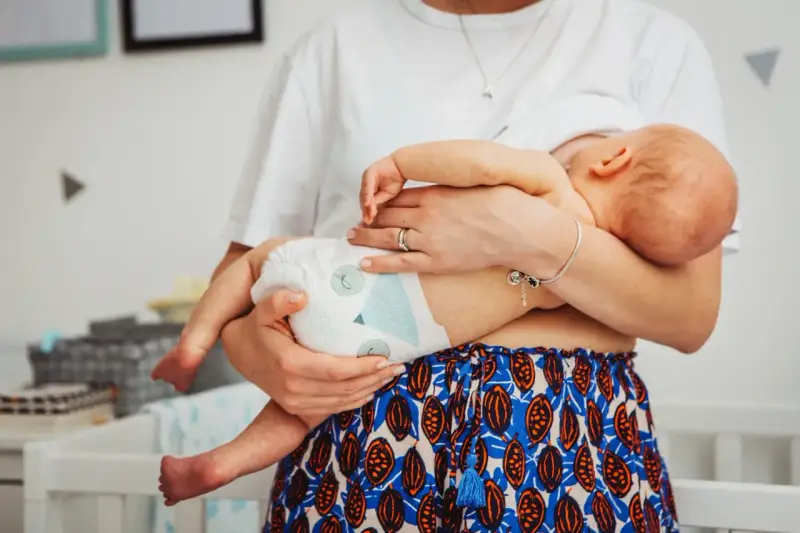 Mama tuli noworodka w pieluszce, idealnie jak ubierać noworodka latem. Lekkie ubranko i pieluszka to klucz do komfortu.