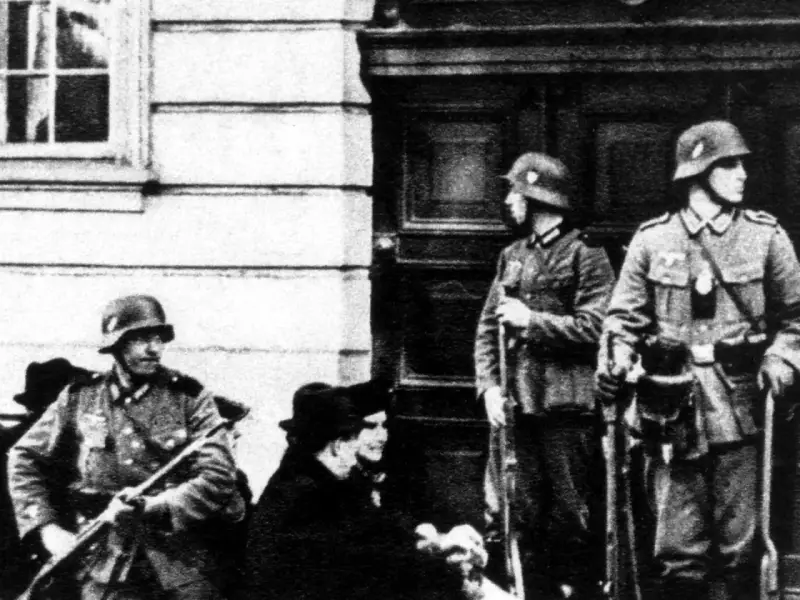 Soldaten der Gestapo stehen Wache. Ein Mann mit Gewehr im Vordergrund, zwei weitere im Hintergrund.
