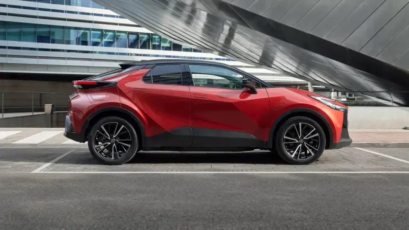 Czerwona Toyota C-HR Hybrid na tle nowoczesnego budynku. Zastanawiasz się, ile kosztuje Toyota C-HR Hybrid?