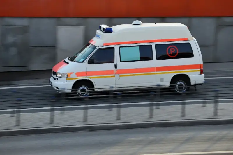 Biała karetka z pomarańczowymi pasami pędzi na sygnale. To pojazd uprzywilejowany, który może brać udział w kursie na pojazdy uprzywilejowane.