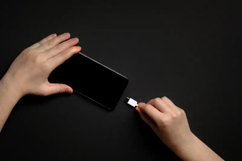 Dwie dłonie trzymają smartfon i biały kabel USB-C. Zastanawiasz się, do ilu procent ładować telefon, by zadbać o jego baterię?