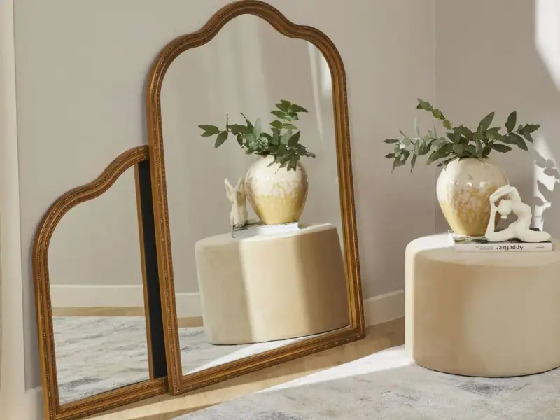 Dos espejos dorados, uno grande y otro pequeño, apoyados en la pared. Ideas para como colocar espejos pequeños en la pared.